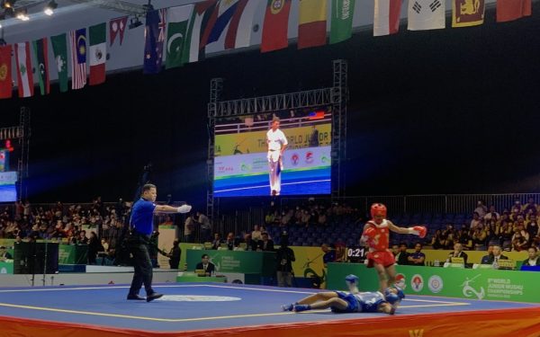 Laga wushu sanda: petarung merah menjatuhkan lawan biru di arena kejuaraan internasional
