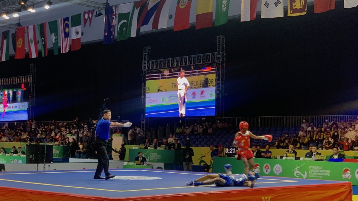 Laga wushu sanda: petarung merah menjatuhkan lawan biru di arena kejuaraan internasional