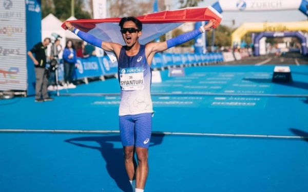 Robi Syianturi, pelari terbaik Asia Tenggara di marathon Asian Games 2026, berselebrasi dengan bendera Indonesia