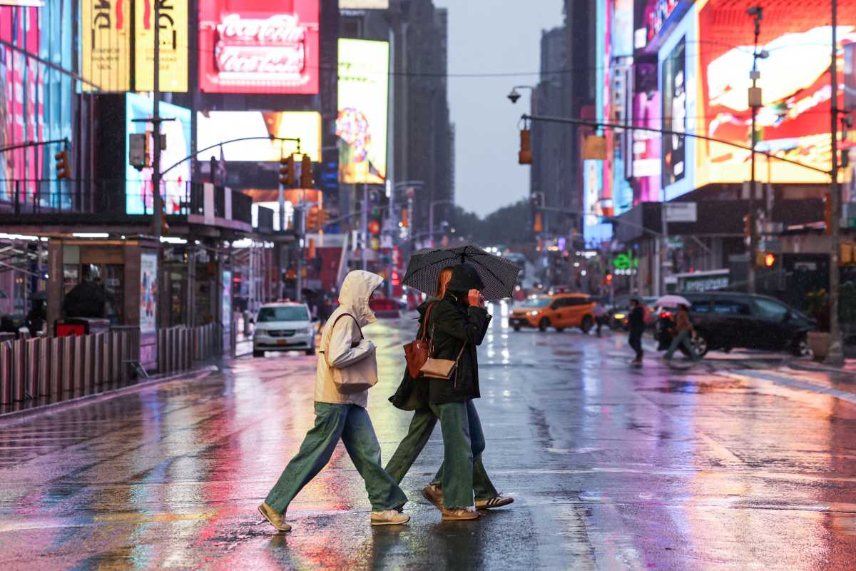 Dua orang menyeberangi persimpangan kota dengan payung di tengah hujan dan lampu jalan
