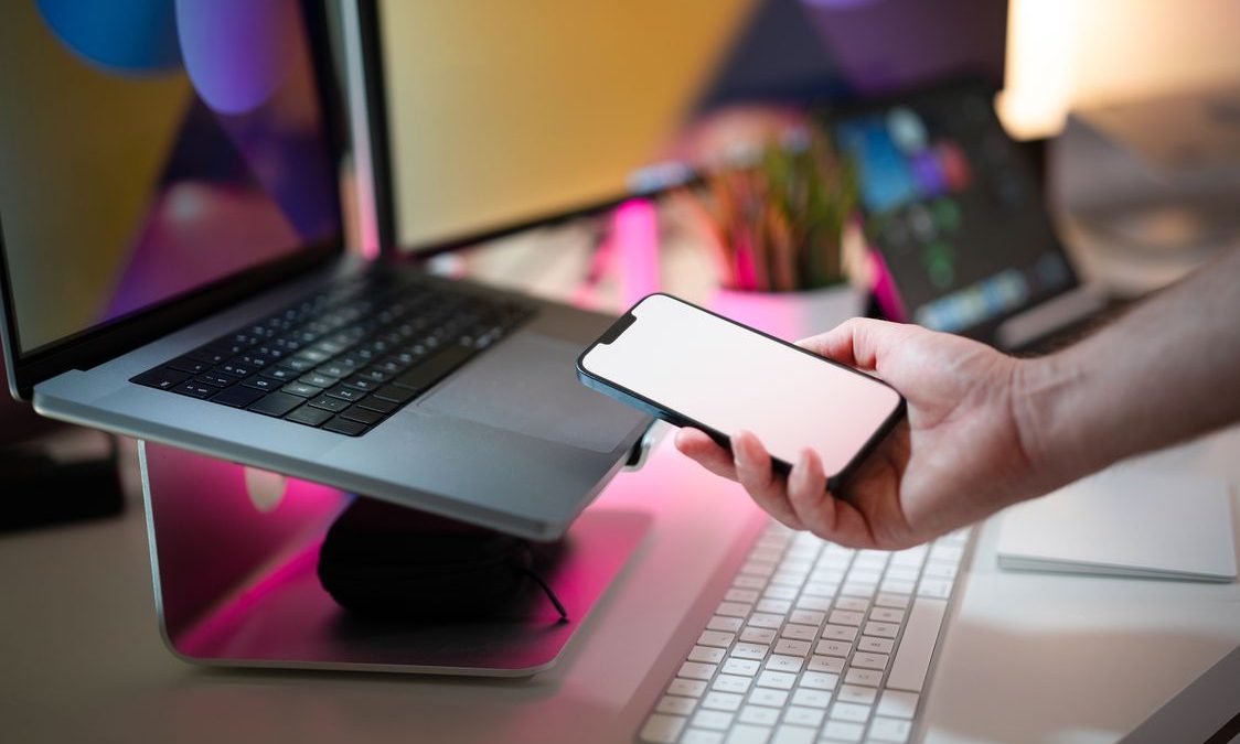 Seseorang memegang ponsel di dekat laptop di meja kerja