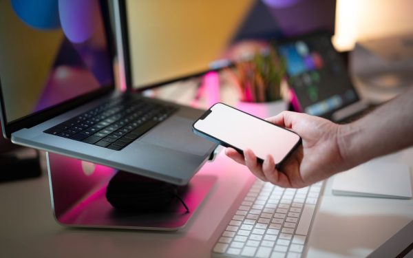 Seseorang memegang ponsel di dekat laptop di meja kerja