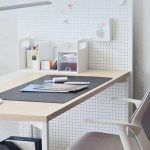 Meja kerja putih minimalis dengan papan pegboard, lampu meja, dan buku catatan