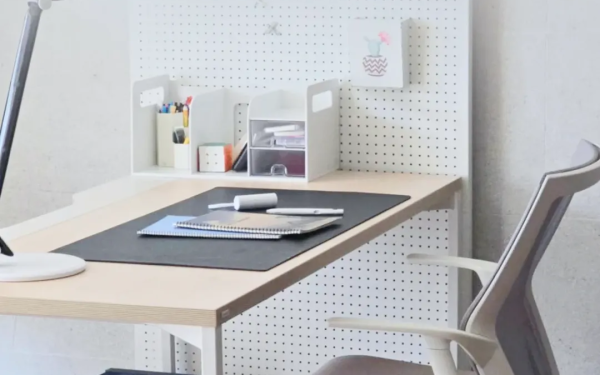 Meja kerja putih minimalis dengan papan pegboard, lampu meja, dan buku catatan