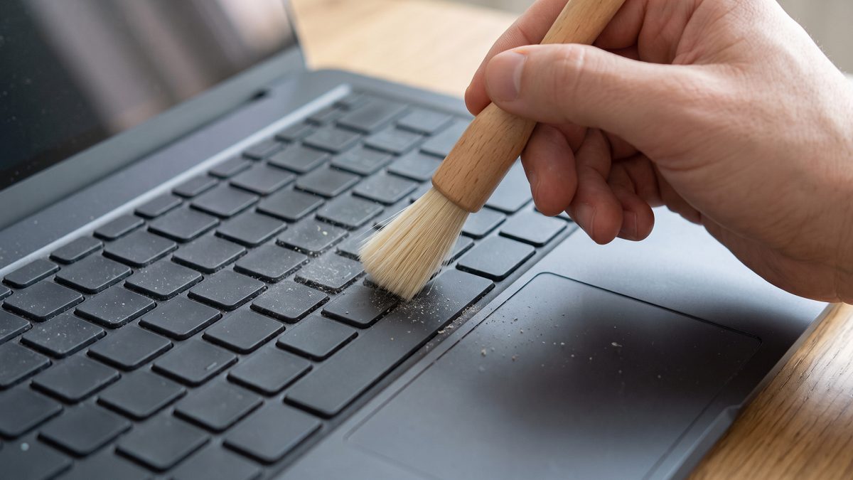 Tangan menyikat keyboard laptop dengan kuas