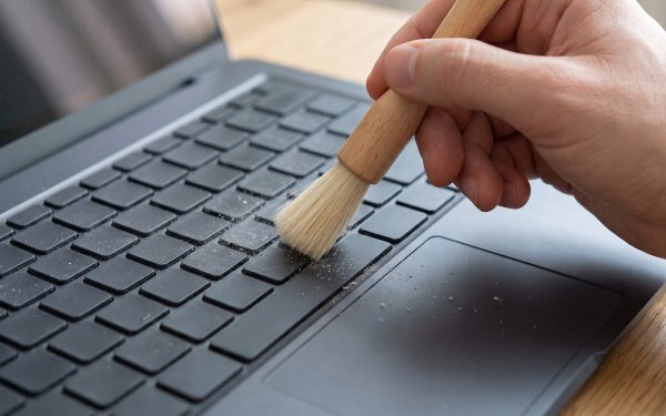 Tangan menyikat keyboard laptop dengan kuas