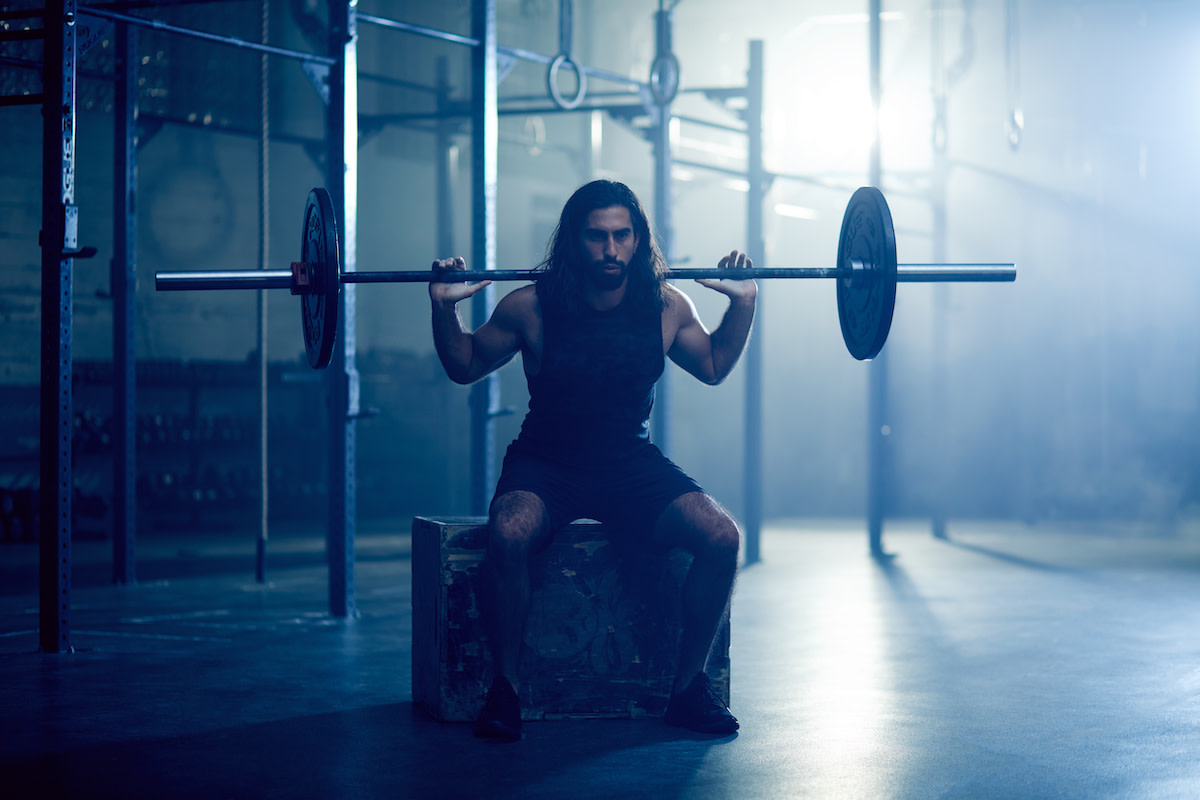 Seseorang berlatih squat dengan beban di gym yang redup