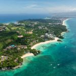 Pemandangan udara garis pantai pulau tropis dengan laut biru kehijauan dan hutan rimbun