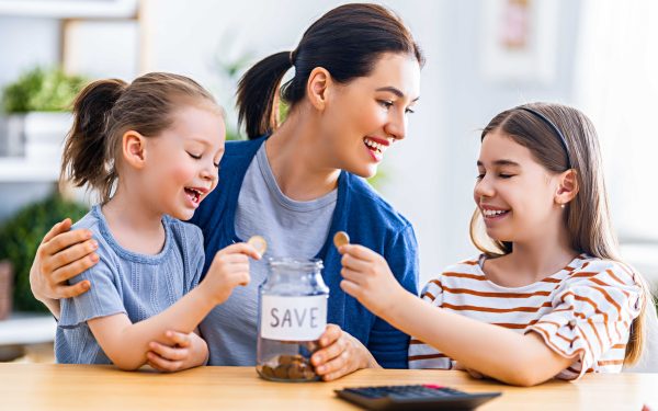 Ibu dan dua anak menabung koin ke stoples kaca bertuliskan SAVE di atas meja