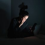 Wanita menggunakan ponsel di ruangan gelap dengan layar menyala
