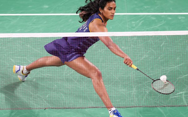 Atlet bulu tangkis memukul smash di lapangan indoor