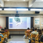 Peserta muda mengikuti seminar di aula menghadap layar presentasi