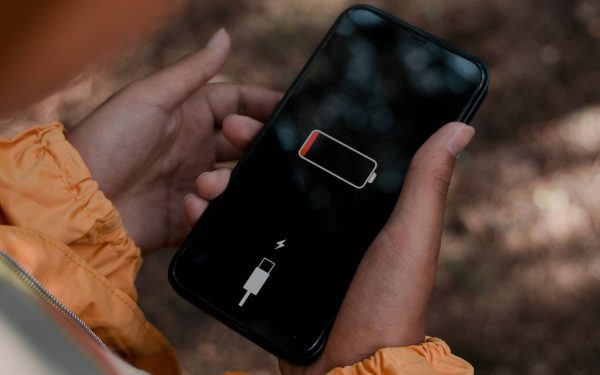 Tangan memegang ponsel dengan ikon baterai di layar