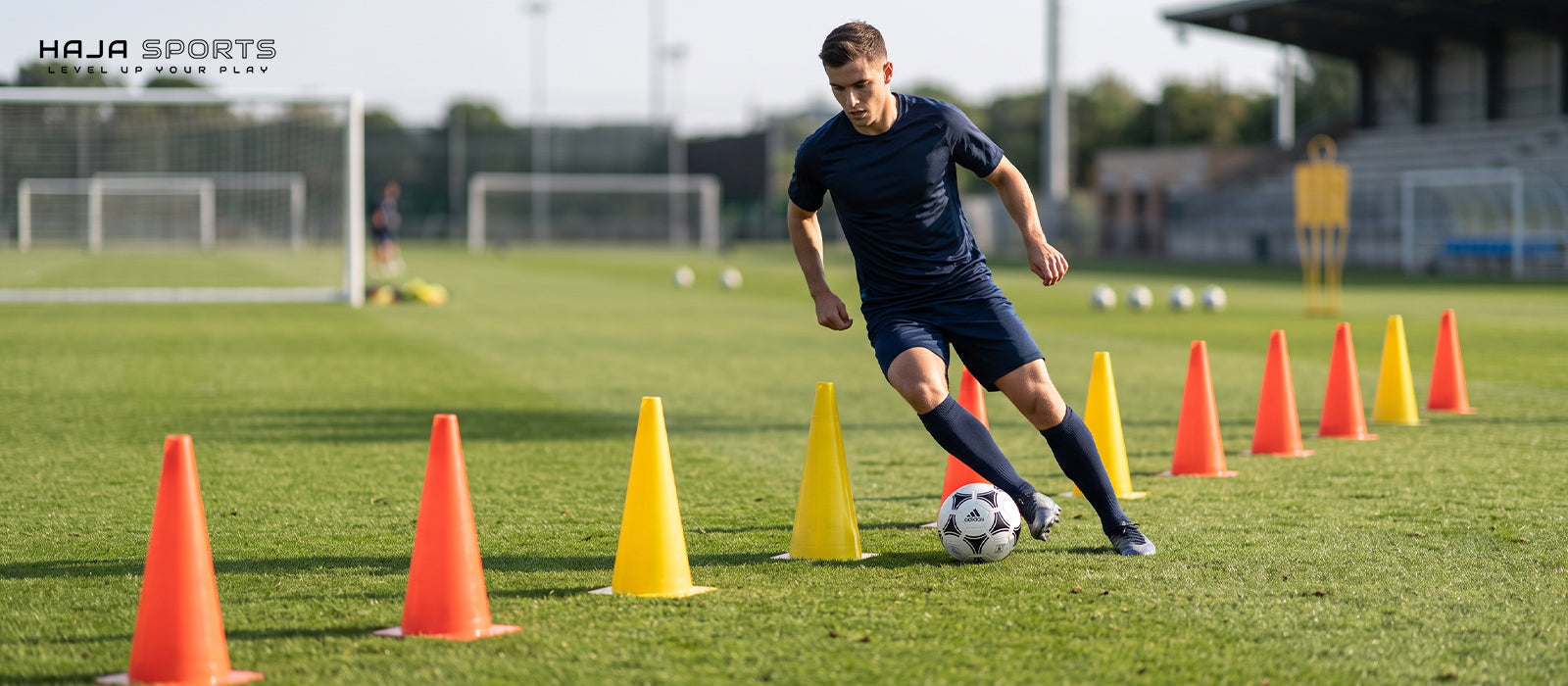 Pemain muda membawa bola melewati kerucut latihan di lapangan sepak bola
