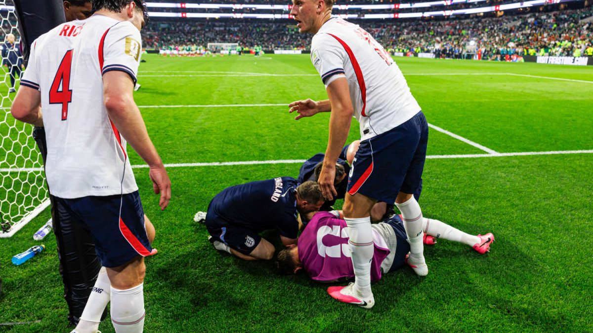 Pemain sepak bola berjersey putih merayakan gol di depan gawang dengan latar tribun penuh