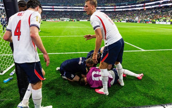 Pemain sepak bola berjersey putih merayakan gol di depan gawang dengan latar tribun penuh