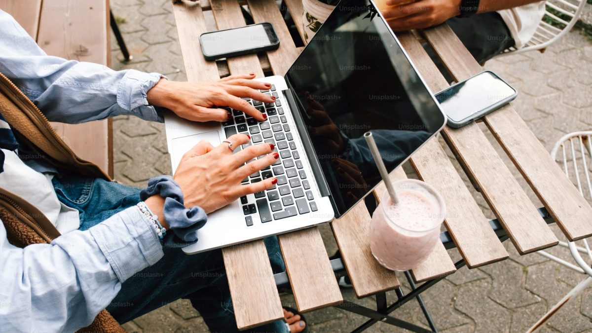 Seseorang bekerja dengan laptop di meja kafe luar ruangan