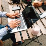 Seseorang bekerja dengan laptop di meja kafe luar ruangan