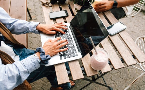 Seseorang bekerja dengan laptop di meja kafe luar ruangan