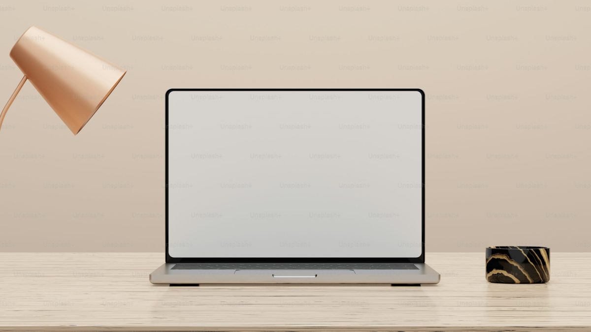 Laptop modern layar kosong di meja kayu bersama lampu tembaga dan cangkir