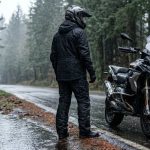 Pengendara motor dengan jas hujan melintasi jalan basah